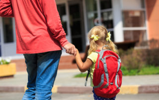 A photo of a father walking little daughter with backpack to school or daycare