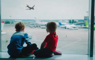 This image accompanies a family law article called "CHILD TAKEN OVERSEAS - WHAT CAN YOU DO?". The image features two children looking at airplanes at the airport.