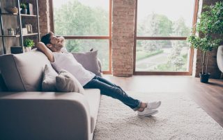 Profile photo of a guy sitting on a cosy sofa holding hands behind his head relaxing and ready to start new life after a divorce