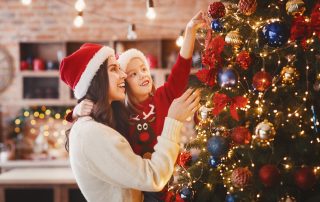 Accompanying image to an article by Michael Lynch Family lawyers. Mother and daughter in Santa hats putting decorations on xmas tree, festive kitchen interior