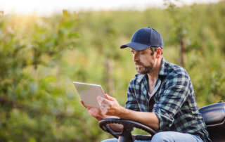 Image of a mature farmer with tablet sitting on mini tractor outdoors accompanying family law article "Rural families in family law settlements"